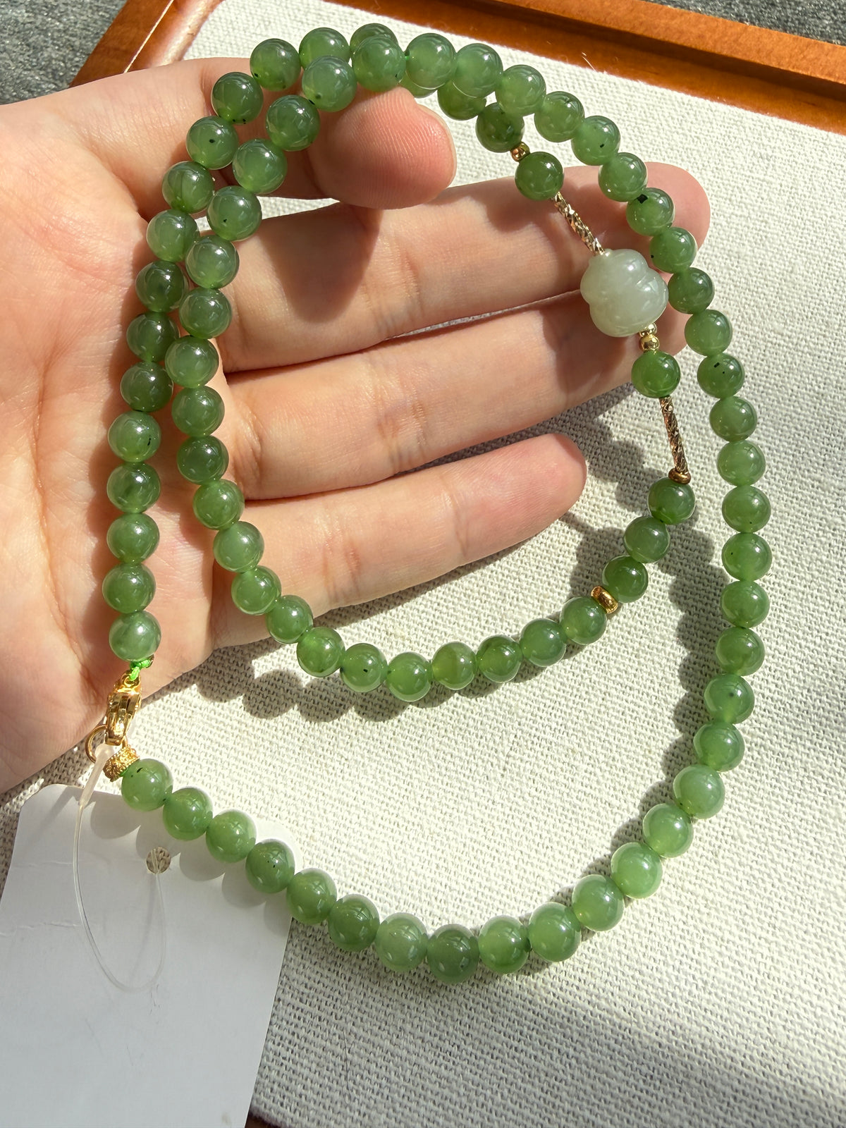 Green hetian jade bead necklace with white carved accent, held in hand