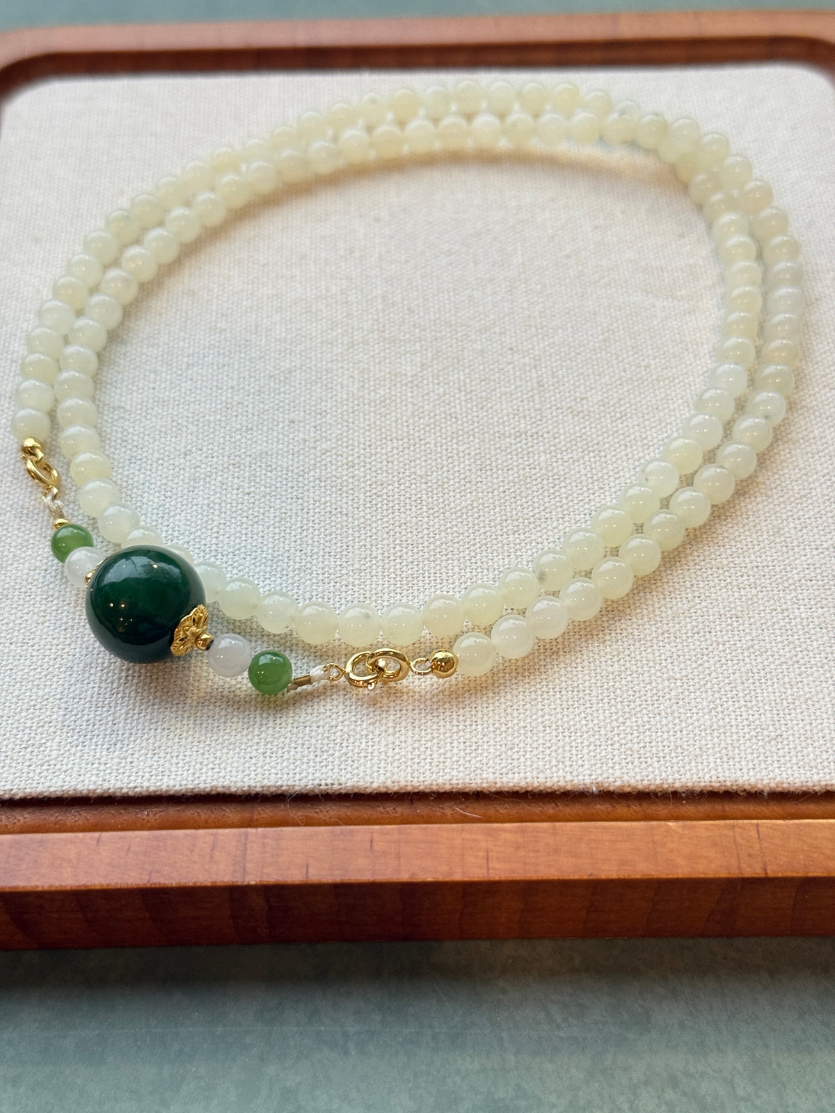 White hetian jade bead necklace with dark green center bead, laid flat