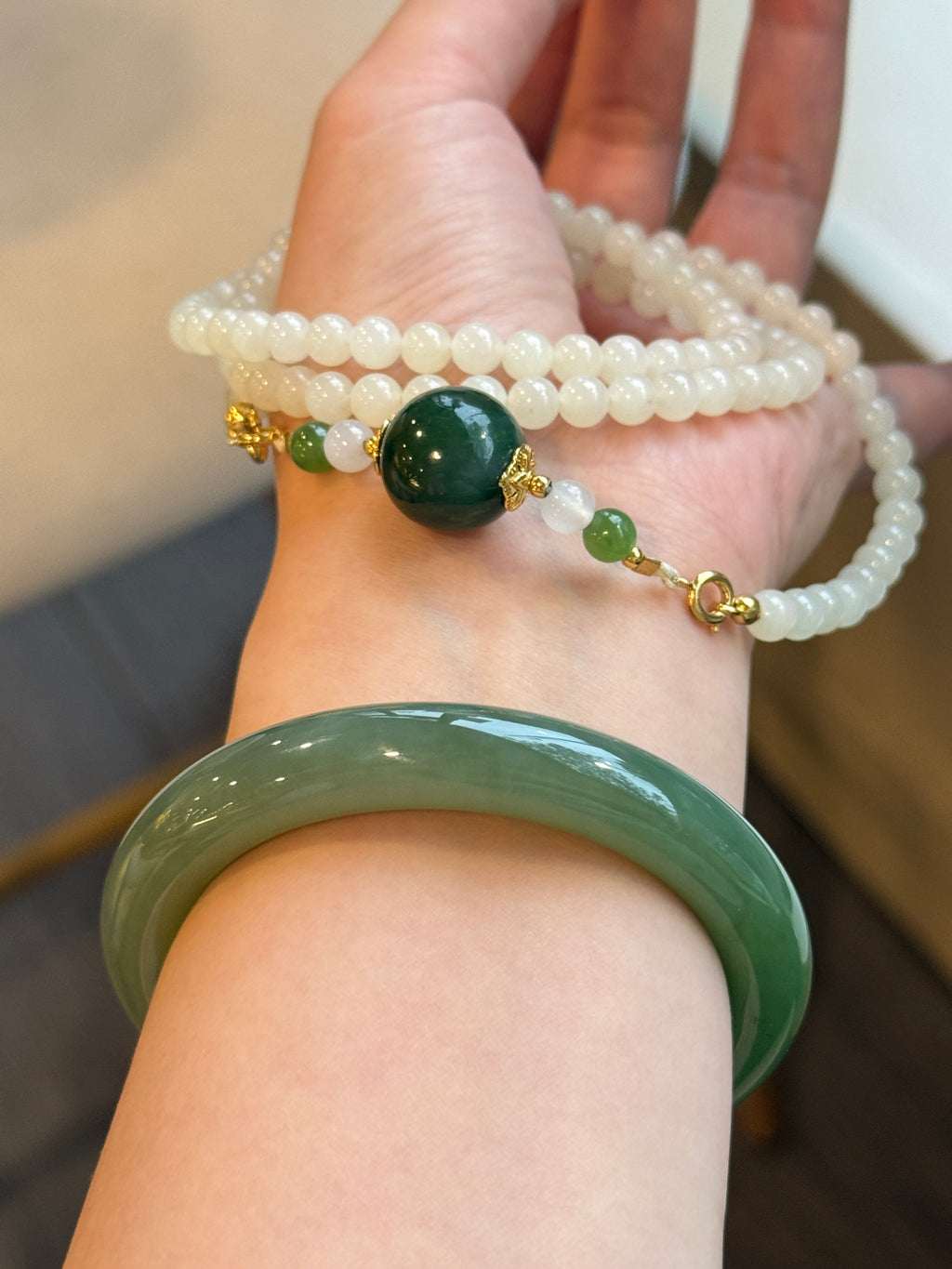 White hetian jade bead necklace held in hand, worn with grey jadeite bangle
