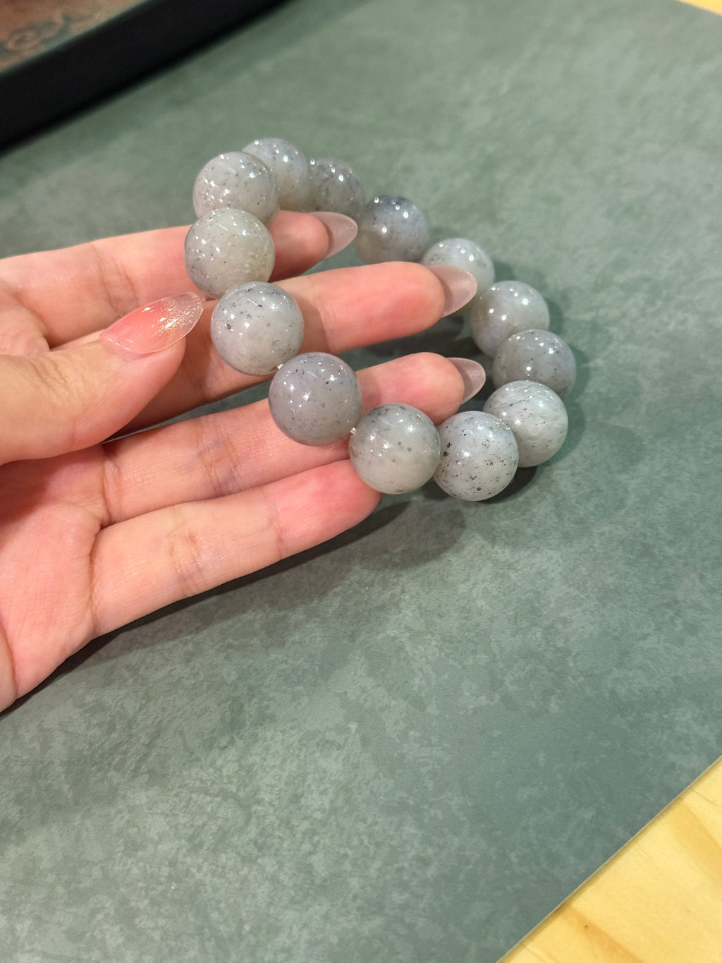 Grey jadeite bead bracelet with black speckles, held in hand