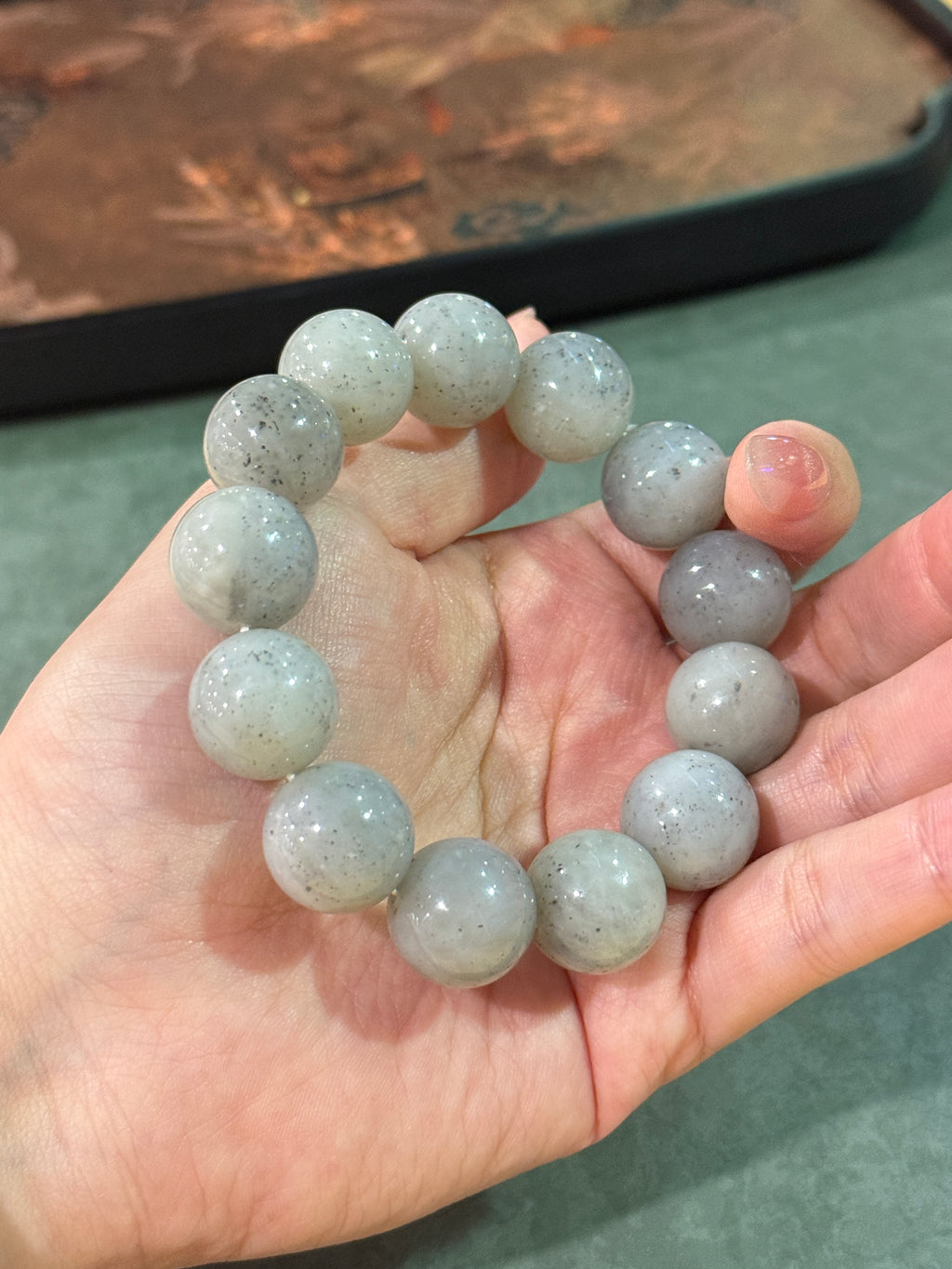 Grey jadeite bead bracelet with black speckles in hand, close-up