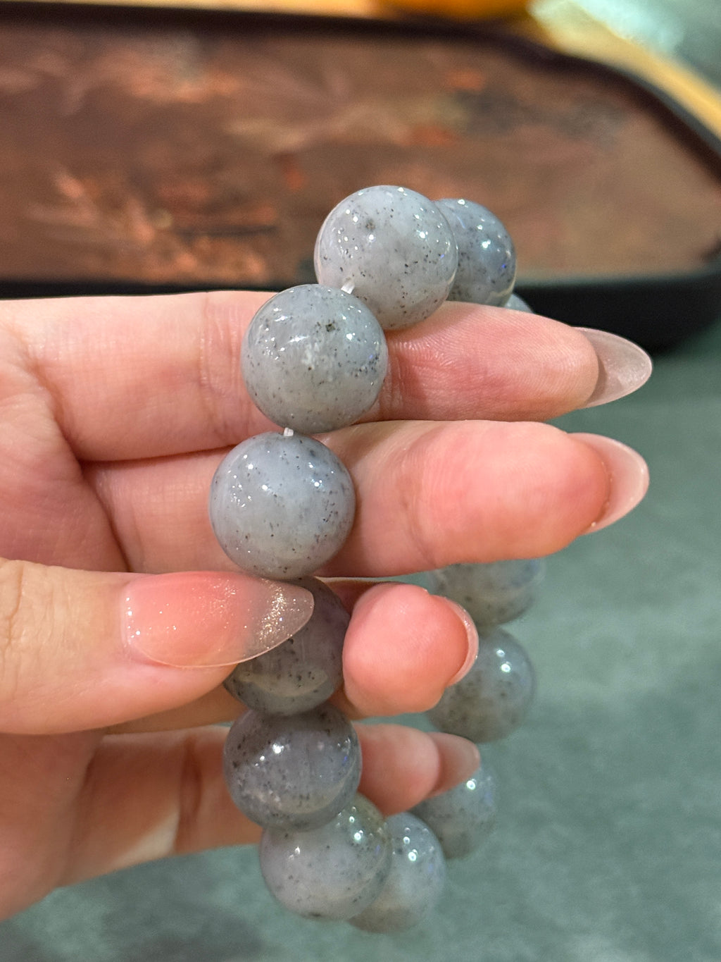 Grey jadeite bead bracelet with black speckles, held between fingers