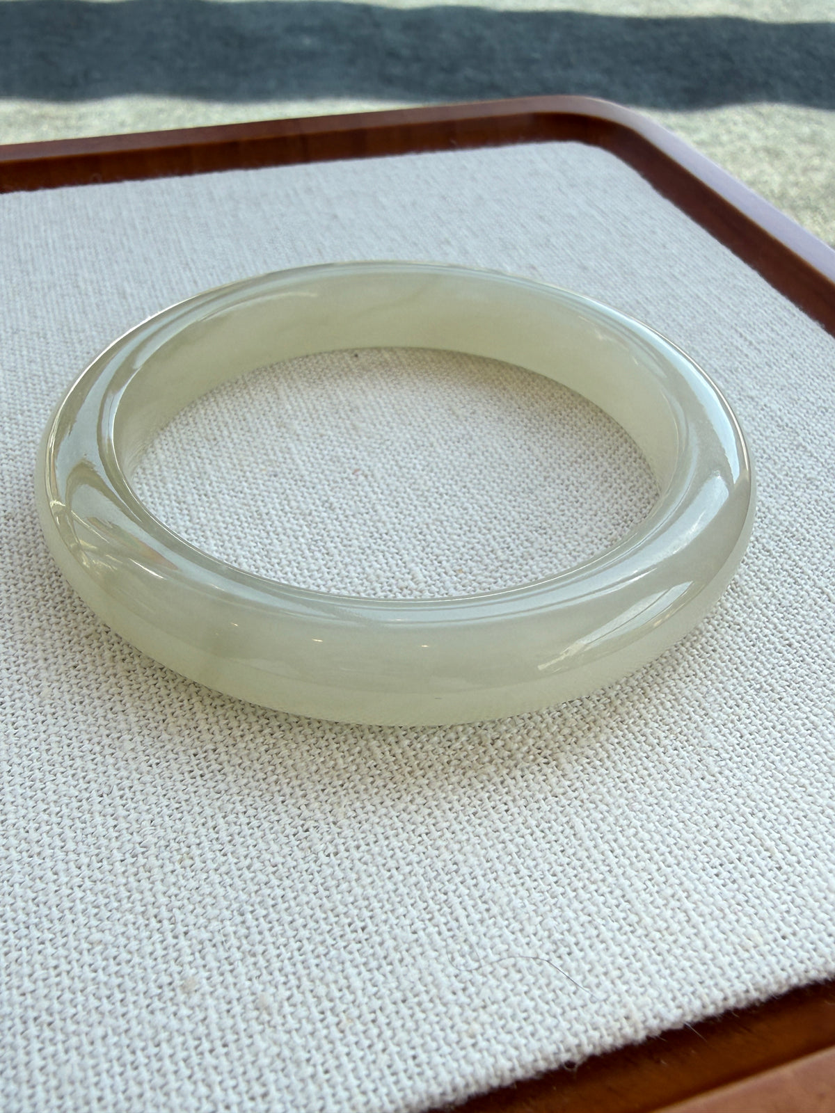 White hetian jade bangle resting on a beige tray — CongCong Jade