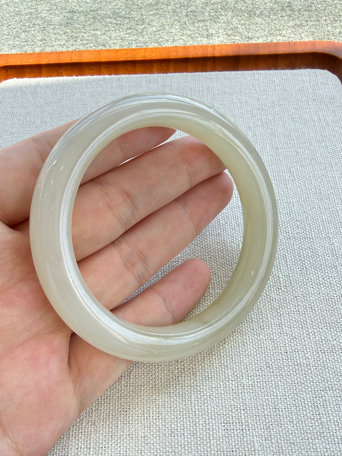 White hetian jade bangle held in hand showing its glow — CongCong Jade
