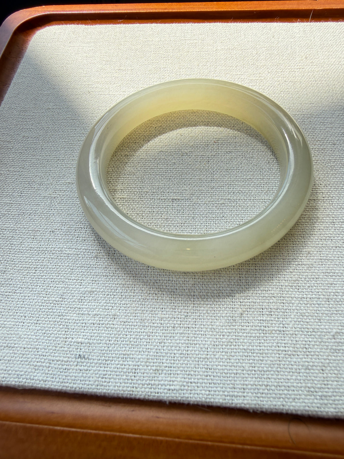 White hetian jade bangle on tray, angled view — CongCong Jade