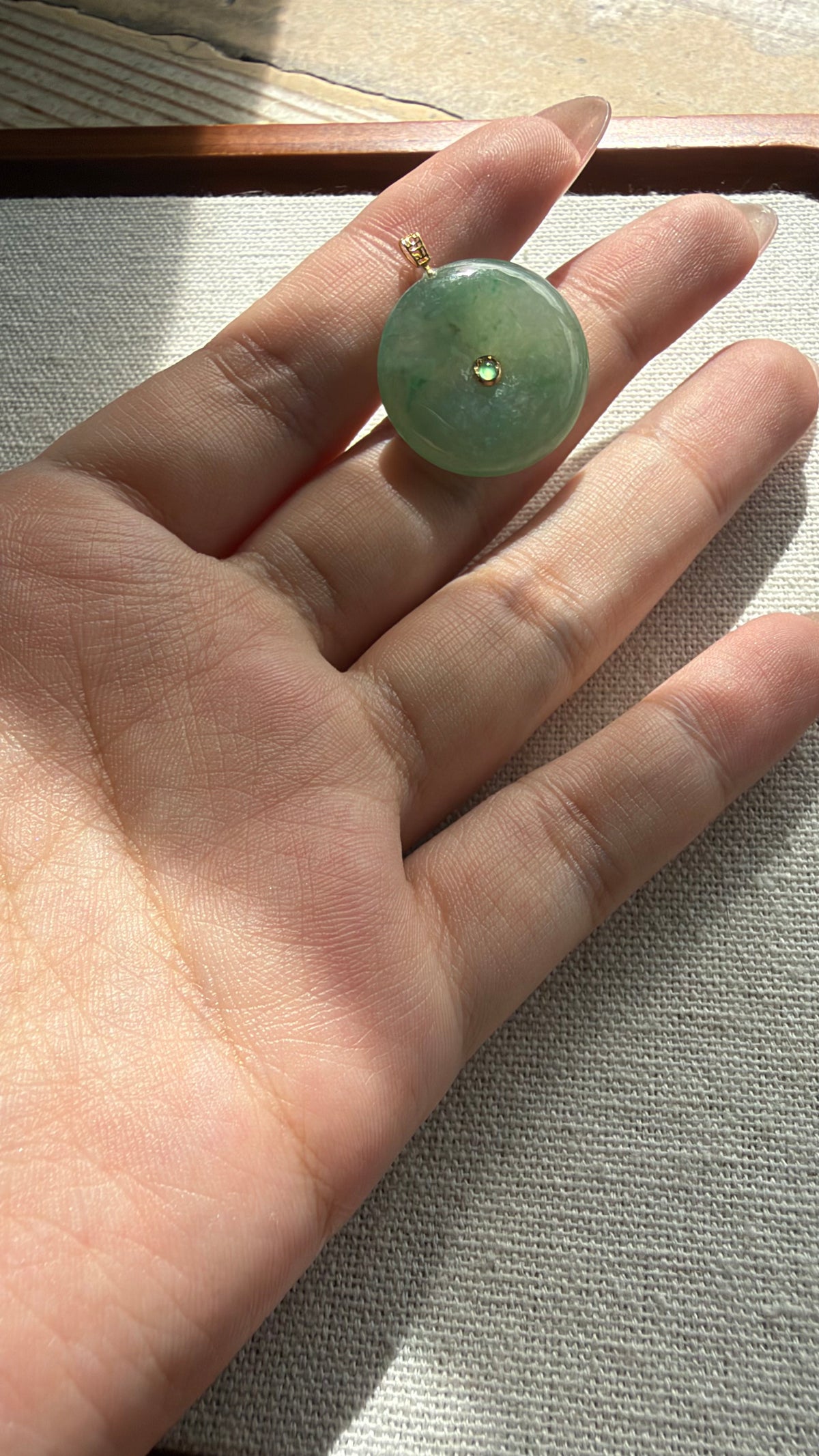 Green jadeite donut pendant held in hand — CongCong Jade